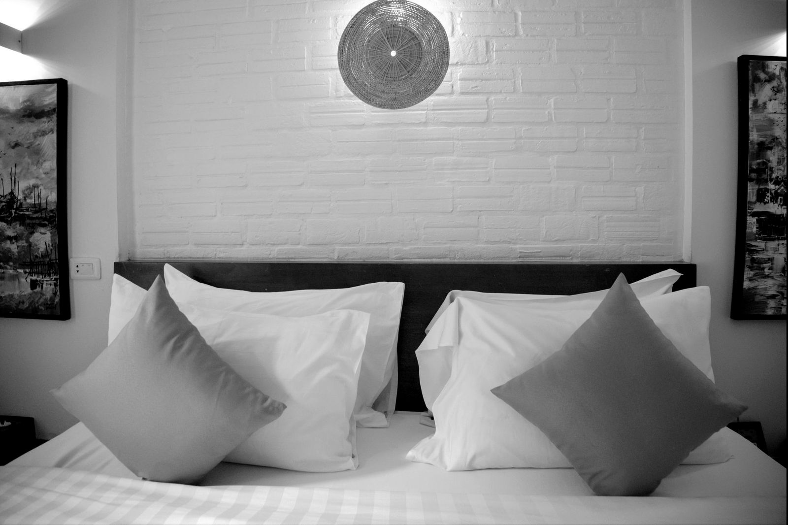A boutique hotel room at Baahu Villa in Siem Reap, Cambodia, with a painted brick wall, dark wood headboard and a woven rattan pendant light